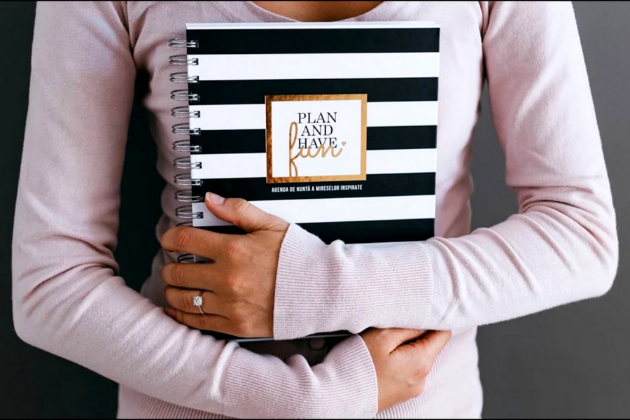 Mireasă ținând agenda de nuntă „Plan and Have Fun”, ideală pentru planificarea detaliilor evenimentului
